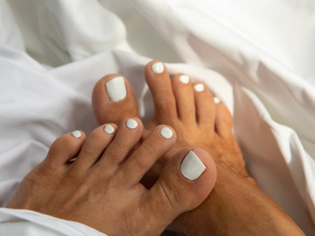 Beautiful shellac pedicure in white on white bed sheets background for the bride. Toes nail polish top view close up. wedding accessories.の写真素材