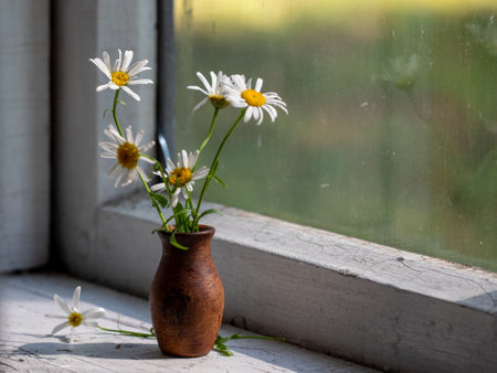 Beautiful retro still life with chamomile flowers in clay jug on windowsill of old window of old country house, summer cottage. Close up, copy space. Floral home decor. country life conceptの写真素材