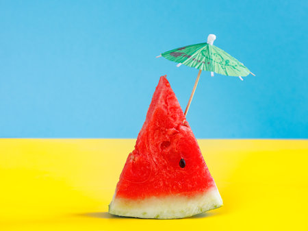 Watermelon slice with cocktail umbrella or sun umbrella on bicolor blue yellow background.の写真素材