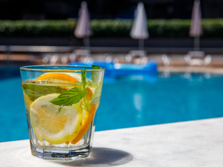 Citrus and mint leaves infused water, cocktail, lemonade in glass near pool. Summer iced cold drinkの写真素材