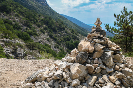 Stack pyramide of stones on top of mountain on background of mountains covered with forests. Croatia, Bol island. Concept of balance and harmony. Stack of zen stones. Teamwork balance conceptの素材 [FY310208596540]