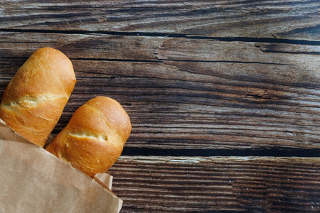 Two loaf of handmade baguette Bread packed in paper on wooden table. Close up, copy space. Top view,...