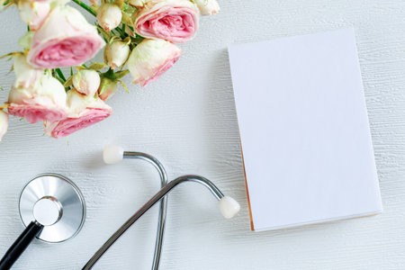 Bouquet of pink rose flowers and stethoscope with empty card notebook on a white background. National Doctor s day greeting card. Top view flat lay, copy spaceの写真素材