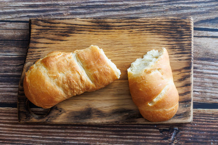 handmade long loaf bread broken off on wooden cutting board against dark wooden background....