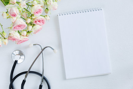 Bouquet of pink rose flowers and stethoscope with empty card notebook on a white background. National Doctor s day greeting card. Top view flat lay, copy spaceの写真素材