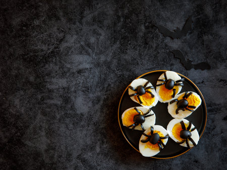 The idea for decorating a table for Halloween funny snack: stuffed eggs with spiders from olives on black plate on black marble background with bats, horizontal, , top view flat lay, copy spaceの写真素材