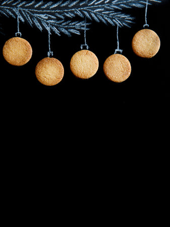 Drawing fir tree branch and Christmas gingerbread cookies like new year balls hanging on black chalk board background. Merry christmas and happy new year, border with copy space, top view vertical.の写真素材
