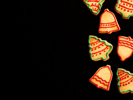 Christmas side border of homemade colorful gingerbread cookies in shape of christmas tree and bell on black background. Xmas greeting card with copy space. View from above. Flat lay.の写真素材