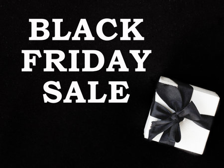Gift box wrapped in white paper and tied with black bow with text Black Friday sale written on black background. concept, top view, minimalismの写真素材