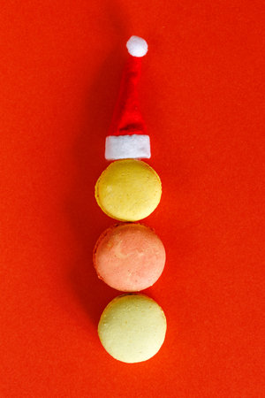 Christmas background with macarons on red, French cakes in shape of snow man with Santa hat on top, recipe for sweet Christmas desserts, minimal composition, verticalの写真素材