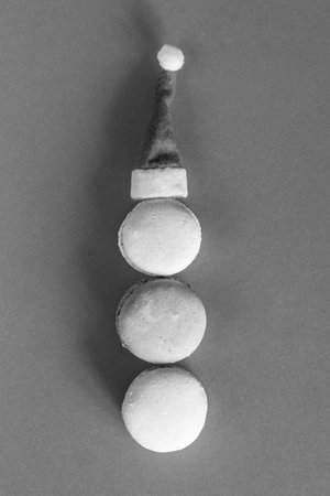 Black and white Christmas background with macarons, French cakes in shape of bw snow man with Santa hat on top, recipe for sweet Christmas desserts, minimal monochrome composition, verticalの写真素材