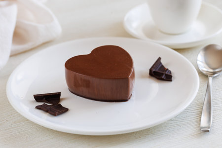 Valentine's day dessert, delicious dark chocolate mousse heart-shaped on white plate with spoon, cup of tea or coffee and napkin.の写真素材