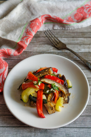 Baked vegetables in sweet and sour sauce on plate. Eggplant, zucchini, paprika and garlic. Healthy vegetarian food, verticalの写真素材