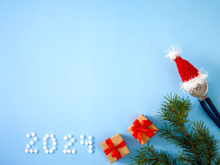 Christmas and New Year medical banner with inscription 2024 made of pills, gift boxes, stethoscope in Santa hat and Christmas tree on blue background. Copy space. Close-up.Top view flatlay copy spaceの写真素材