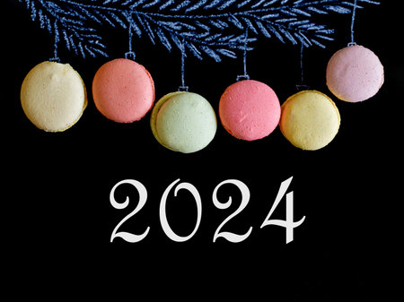 Drawing fir tree branch and Christmas macarons macaroons like new year balls hanging on black chalk board background and inscription 2024. Merry christmas and happy new year, top view flat layの写真素材