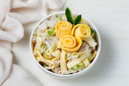 Salad of shredded boiled chicken, fresh cucumber, onion and chopped egg pancakes closeup in bowl on table. Decorated with roses from egg pancakes, Party dinner. Top view from above.の写真素材