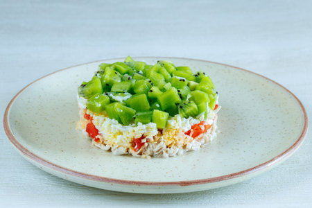 Layered Salad with chicken cheese and kiwi in round shape on a plate on a white tableの写真素材