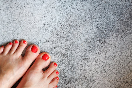 Beautiful womans red nails with beautiful pedicure. Female feet with bright pedicure on grey concrete background. Autumn and winter concept. Top view, copy space, horizontal, close upの写真素材