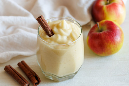 Fresh homemade applesauce, apple puree, mousse, sauce in glass with cinnamon and apples on white table, side view. Organic vegetarian food. Healthy eatingの写真素材
