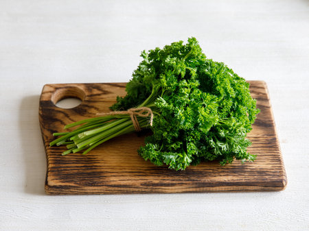 Bunch of raw fresh green curly parsley on wooden cut board on white wooden background, top view close upの写真素材
