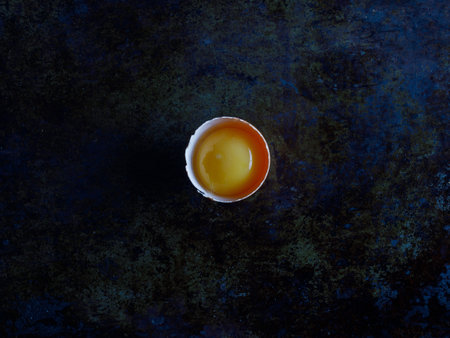Half fresh raw broken chicken egg on dark stone background. Top view of bright yolk, copy space for text or recipe. Breakfast, lunch, easter, cooking concept. Top view from above, flatlay copy spaceの写真素材