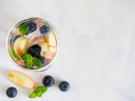 Blueberry and peach infused water, cocktail, lemonade or tea in double glass. Summer iced cold drink with blueberry, ice, peach and mint on gray marble background, copy space, top view flat layの写真素材