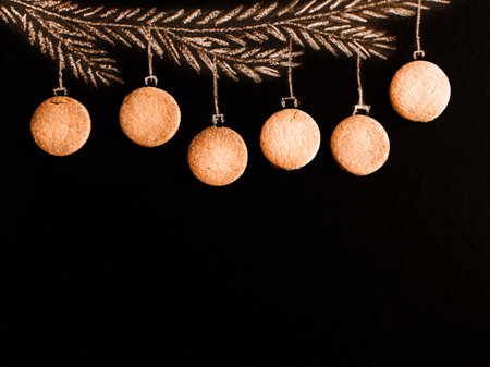 Drawing fir tree branch and Christmas macarons like new year balls hanging on apricot crush trend 2023 color background. Merry christmas and happy new year, border with copy space, top view.の写真素材