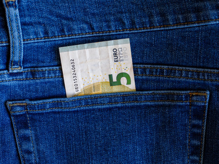 Close up of one five Euro banknote peeking out of blue jeans back pocket. Budget travel or shopping, low earnings, economical crisis, pocket money concept.の写真素材