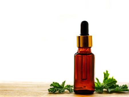 Geranium essential oil in dark glass bottle with fresh scented geranium leaves on old wooden board isolated on white background. Aromatherapy oil, spa massage, mosquito repellent. Copy spaceの写真素材