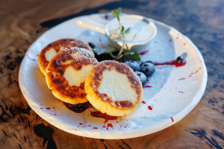 Cottage cheese fritters, curd pancakes or syrniki served with blueberry jam, greek yogurt or sour cream on wooden table. Close up. Healthy calcium breakfast, lunch or snack. Traditional russian foodの写真素材
