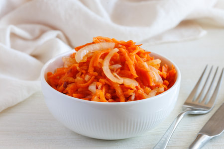 Fresh healthy vegetarian carrot salad with apple, onion and spices in the bowl with fork and knife. Side view, close upの写真素材