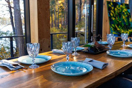 Preparing for party in forest luxury restaurant on river bank. Decorated served table await guests. Decoration Details. large window with wild mountain forest view. Tourism and vacationsの写真素材