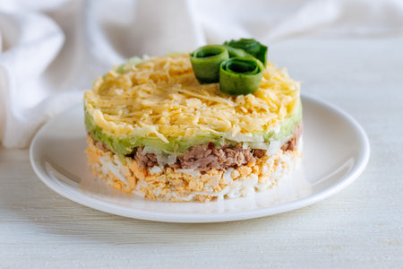 Layer canned tuna, fresh cucumber, boiled egg and cheese salad on white plate on a table. Selective focus. Side view, close upの写真素材
