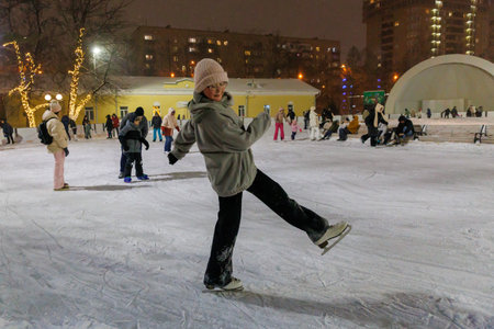 Funny moment fell on the ice skating rink. Holiday and seasonal concept. Teenager ice skating on public ice rink in park in evening.の写真素材