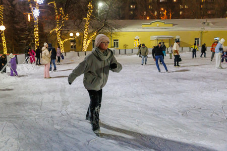 Portrait of young girl ice skating on a large ice rink in public park in evening.の写真素材