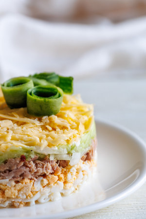 Layer canned tuna, fresh cucumber, boiled egg and cheese salad on white plate on a table. Selective focus. Side view, vertical, close upの写真素材