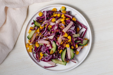 Healthy fresh salad with red cabbage, cucumber, carrot, ham and corn on a plate on white wooden table. Bright food top view close upの写真素材
