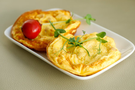 Two small stuffed omelette with ham, tomato and peas micro green on white plate on gray background.の写真素材