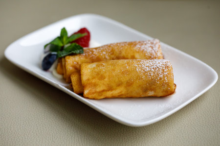 Rolled up stuffed thin pancakes with sourcream, mint leaf and raspberry on white background.の写真素材