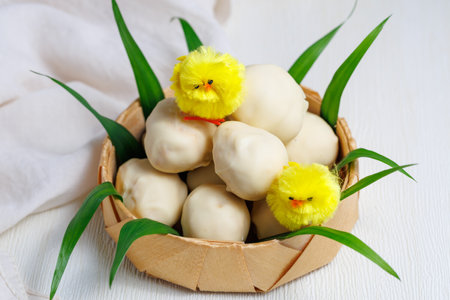 White chocolate easter eggs. Sweet candy eggs in nest on white table with yellow chicks and grassの写真素材