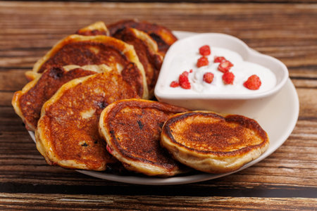 Pancakes with sour cream on the wooden table. Russian fritters oladyi with berries. Close up, rustic, heart shaped bowl.の写真素材