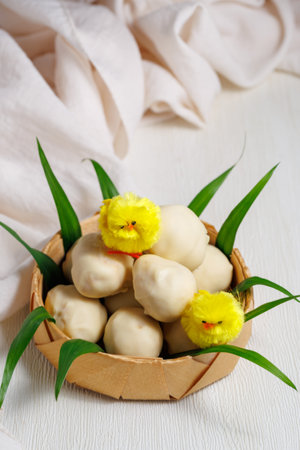 White chocolate easter eggs. Sweet candy eggs in nest on white table with yellow chicks and grass. Verticalの写真素材