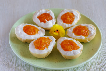 homemade white chocolate half easter egg, stuffed with cream cheese and orange jam looks like whites and yolk. On plate with chick. Easter egg with pudding cream, Easter dessert. Easter conceptの写真素材