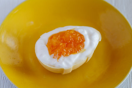 One homemade white chocolate half easter egg stuffed with cream cheese and orange jam looks like white and yolk. On yellow plate close up. Easter egg with pudding cream, Easter dessert conceptの写真素材