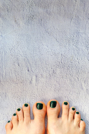 Beautiful womans green emerald nails with beautiful pedicure. Female feet with bright pedicure on grey concrete background. Christmas and summer concept. Top view, copy space, vertical, close upの写真素材
