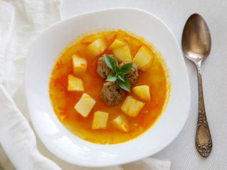 Delicious homemade meatball soup with vegetables potato, carrot and onion in white ceramic bowlの写真素材