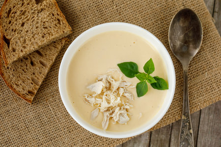 bowl of homemade cauliflower cream soup with chicken and basil with two slices of dark bread on canvas napkinの写真素材