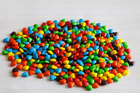 Handful of colorful sweet little glazed multicolored chocolate bonbons candies, m and ms with heart shapes, isolated on white backgroundの写真素材