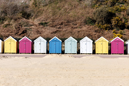Row of wooden colorful beach huts in spring in sandy seafront with cliffs in background in Bournemouth, UK. South coast of England. No people.の写真素材