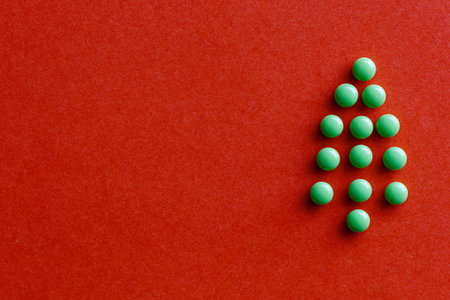 Round green tablet in shape of Christmas tree on red background. Unusual tree. Christmas and New Year medical concept. Copy spaceの写真素材